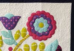 Sue Nickels shares her signature technique for assembling a vibrant, floral appliqué quilt top. Each piece of appliqué uses just a bit of fusible web to keep it in place, and is then secured permanently with machine blanket stitching.